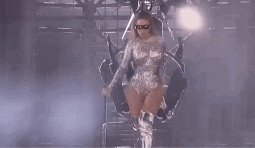 a woman in a silver bodysuit and mask is standing on a stage .