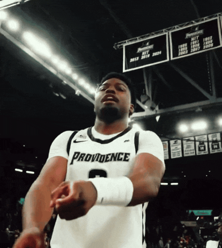 a basketball player wearing a providence jersey stands in front of a scoreboard