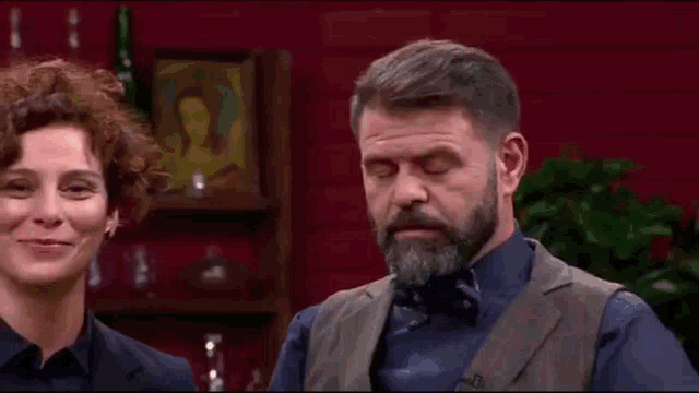 a man with a beard and bow tie is standing next to a woman with curly hair .