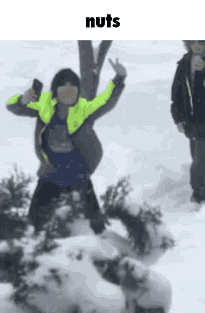 a boy is standing in the snow with his arms in the air and the word nuts above him .