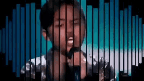 a young boy is singing into a microphone in front of a grid .