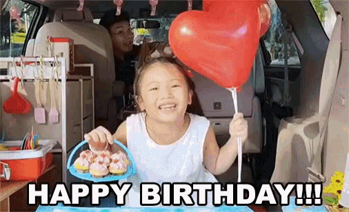 a little girl is holding a red heart shaped balloon and a basket of cupcakes in the back of a van .