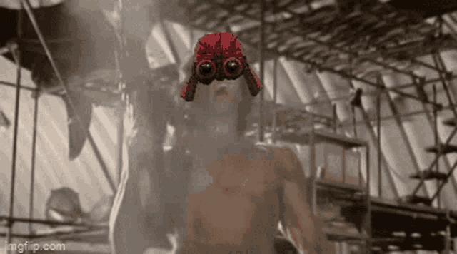 a shirtless man wearing a red hat and goggles is standing in a building .