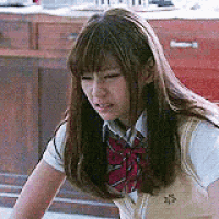a girl in a school uniform is sitting on the floor and looking down .