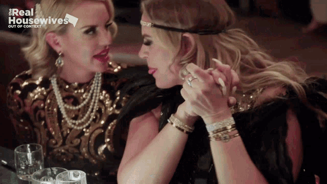 two women are sitting at a table with a real housewives logo on the bottom