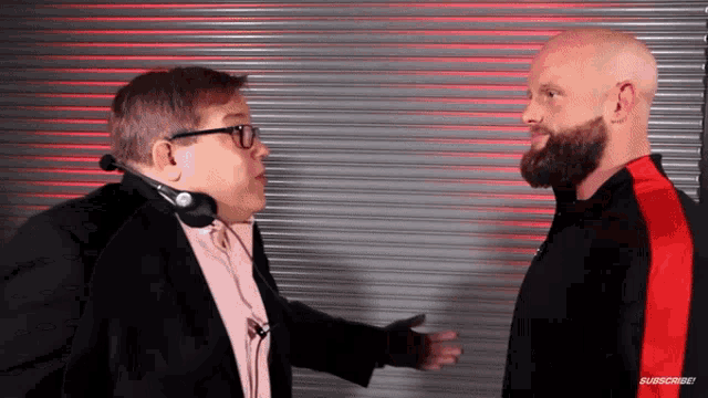 a man wearing glasses and a headset talks to another man with a beard