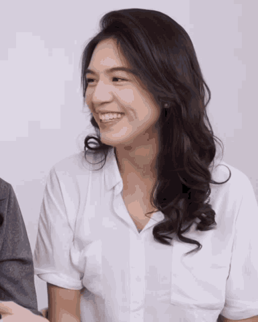 a woman in a white shirt is smiling and looking away