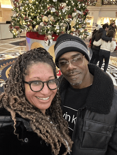 a man and woman pose in front of a christmas tree
