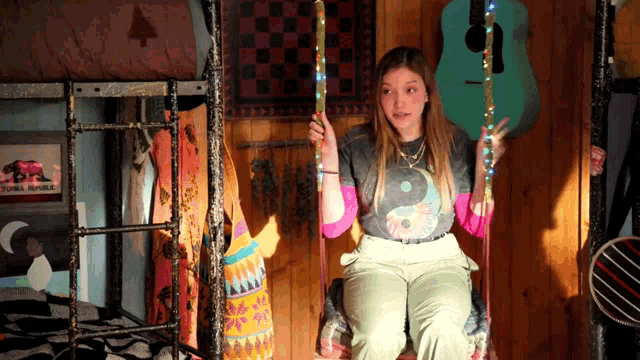 a girl is sitting on a swing in front of a guitar
