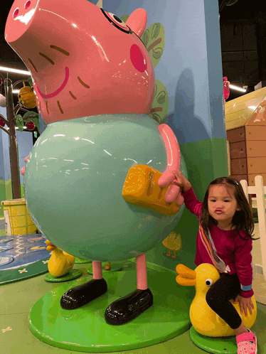 a little girl sits on a yellow duck next to a statue of peppa pig
