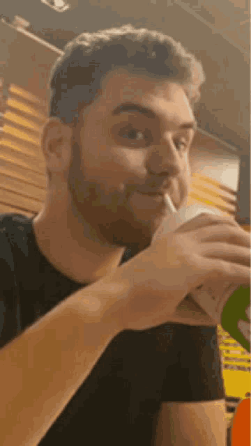 a man with a beard is drinking a milkshake with a straw .