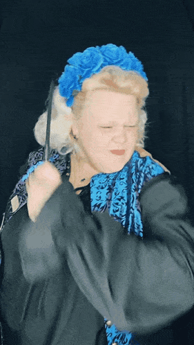 a woman wearing a blue headband and a black jacket holds a wand