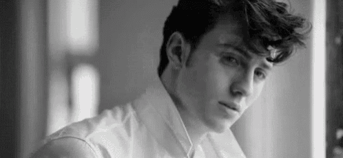 a black and white photo of a young man looking at the camera .