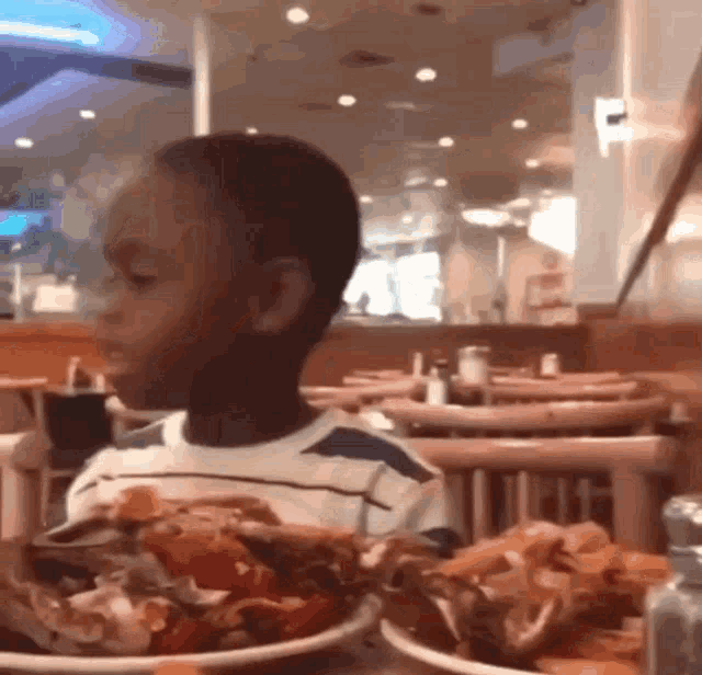 a young boy sitting at a table with a plate of food
