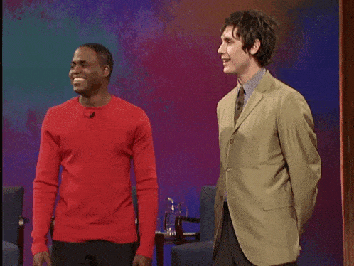 a man in a red sweater is talking to another man in a green suit