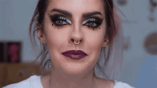 a woman with purple lipstick and a nose ring looks at the camera