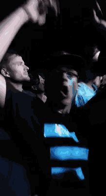 a group of people are sitting in a dark room and one of them is wearing a blue shirt