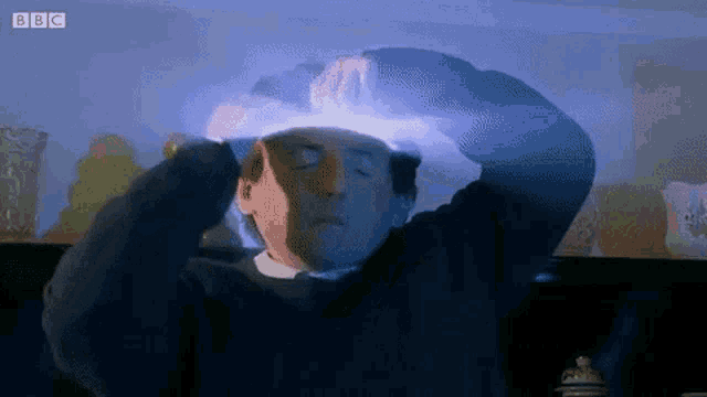 a man is holding his head with his eyes closed and a light coming out of it .