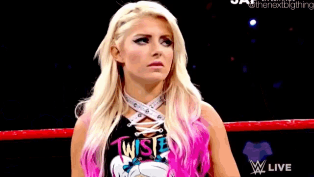 a woman with blonde hair and pink highlights is standing in a wrestling ring and making a funny face .