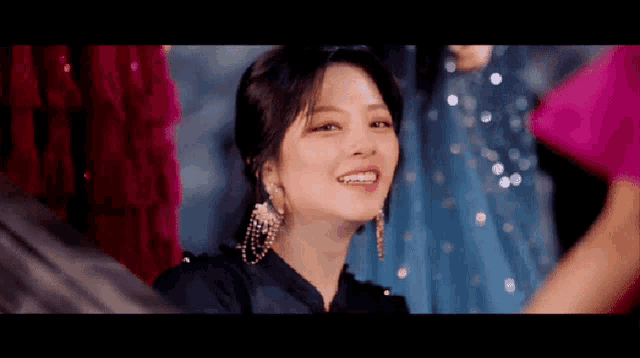 a woman wearing a black dress and earrings is smiling and looking at the camera .
