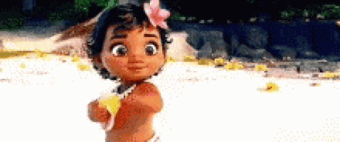 a little girl with a flower in her hair is standing on a beach holding a flower .