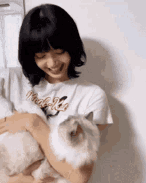 a woman is holding a cat in her arms and smiling at it .