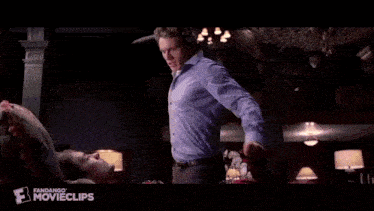 a man in a blue shirt is standing in a room with lamps and orchids .