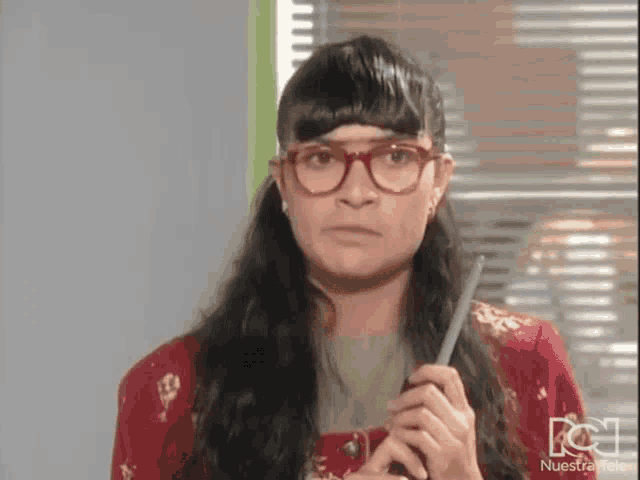 a woman wearing glasses and a red shirt is holding a pen in her hand .