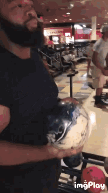 a man with a beard is holding a bowling ball in a bowling alley with imgplay written on the bottom