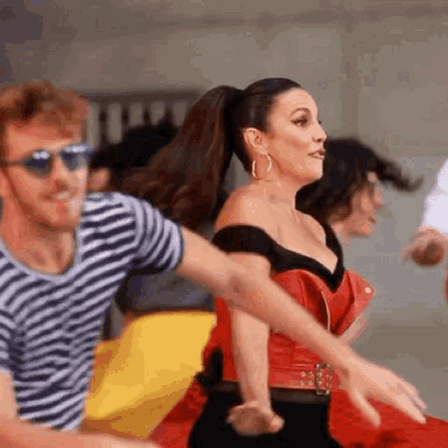 a woman in a red dress is dancing with two men in striped shirts .