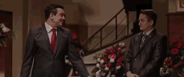 two men in suits are standing next to each other in front of a staircase .