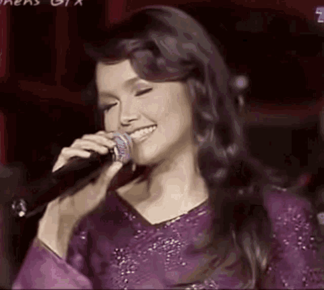 a woman in a purple dress is singing into a microphone on stage .