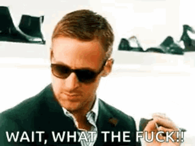 a man wearing sunglasses and a suit is holding a cell phone and says `` wait , what the fuck ! ''