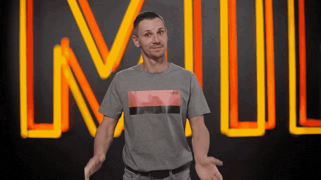 a man wearing a grey levis t-shirt stands in front of a neon sign