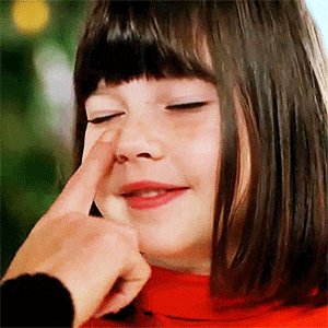 a little girl is being touched by someone 's finger to her nose .