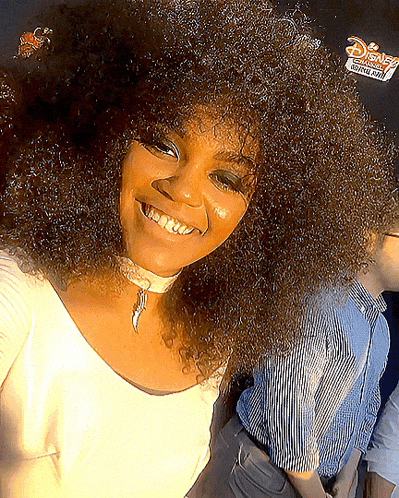 a woman with curly hair smiles in front of a disney sign