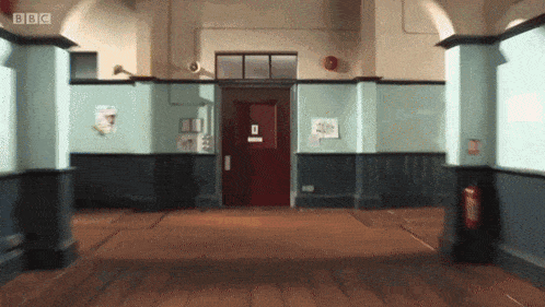 a hallway with a red door and a bbc logo on the wall