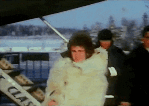 a man in a fur coat is standing in front of a staircase that says ct on it .