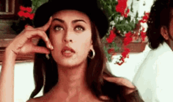 a woman wearing a black hat and earrings is looking at the camera .