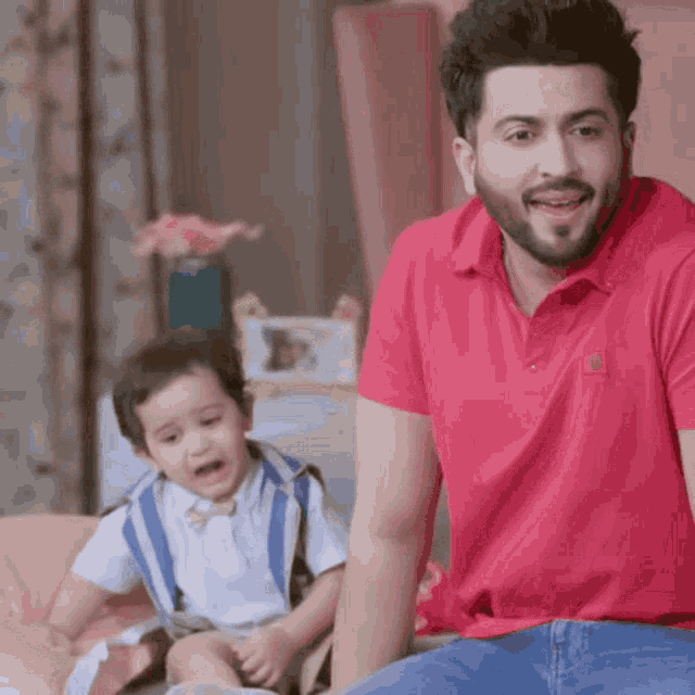 a man in a red shirt is sitting next to a baby