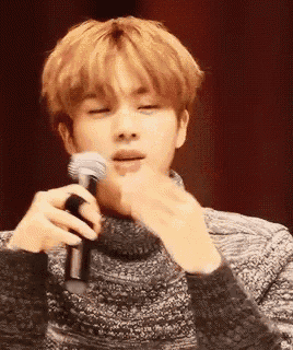 a young man in a sweater is holding a microphone in front of his face