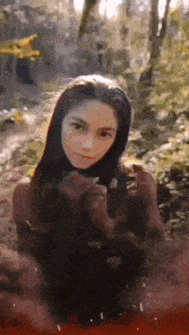 a woman is standing in the woods looking at the camera .