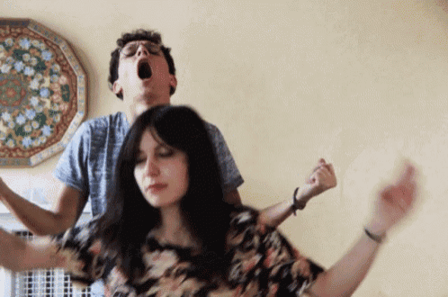 a man and a woman are dancing with their arms outstretched in front of a wall with flowers on it