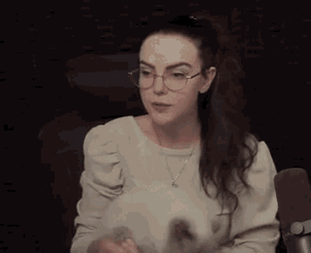 a woman wearing glasses and a ponytail is holding a cat in front of a microphone .
