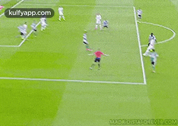 a soccer player is kicking a ball on a soccer field while another player watches .