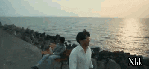 a man in a white shirt is walking along a rocky shoreline near the ocean .