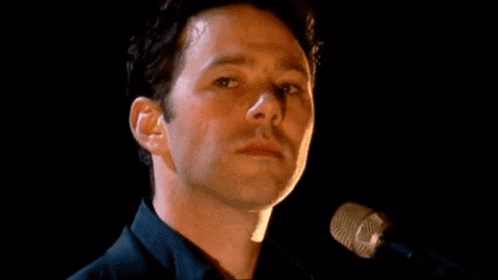a man is standing in front of a microphone looking at the camera .