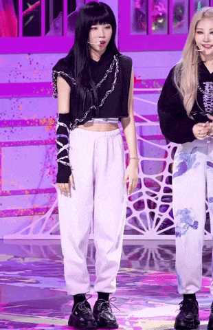 a woman in a black crop top and white sweatpants is standing on a stage with another woman .