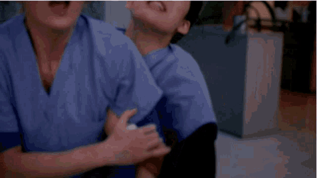 two nurses in scrubs are hugging each other in a hospital room