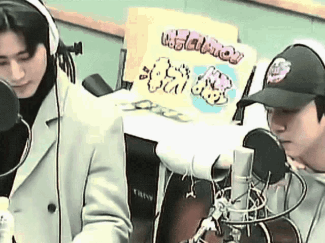 two men wearing headphones and hats are standing in front of a microphone .